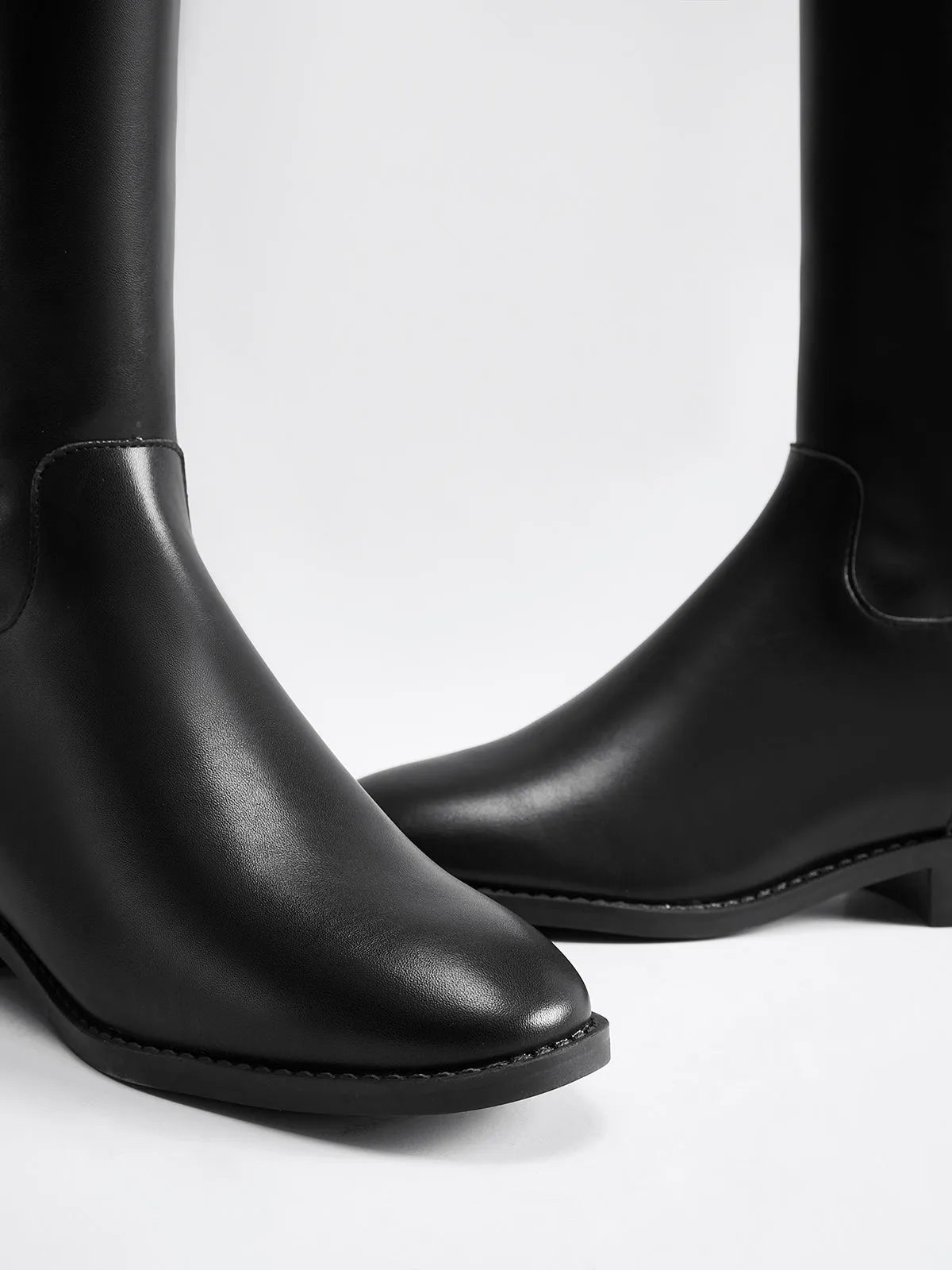Close-up of black riding-style boots showing the rounded toes, stitching and low heel.