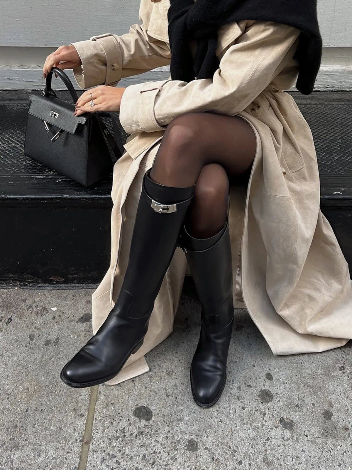 Black knee-high riding boots styled with a beige trench coat and dark tights.