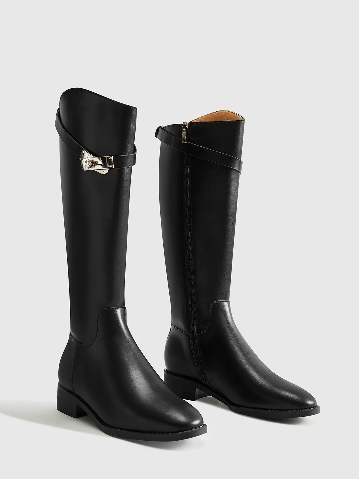 Pair of black knee-high boots showing the buckle straps, side zipper and low heels.